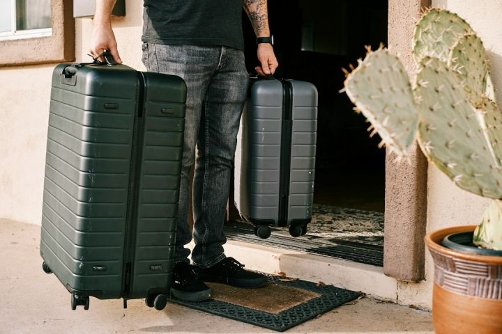 Luggage - man in black denim jeans and black leather shoes standing beside black luggage bag