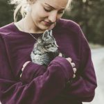 Pet Care - Selective Focus Photography of Woman Wearing Purple Sweater Holding Silver Tabby Cat