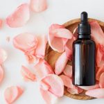 Beauty Essentials - Top view of empty brown bottle for skin care product placed on wooden plate with fresh pink rose petals on white background isolated