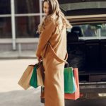 Sustainable Shopping - Full length of cheerful female looking over shoulder while standing near opened trunk of car on parking of shopping mall